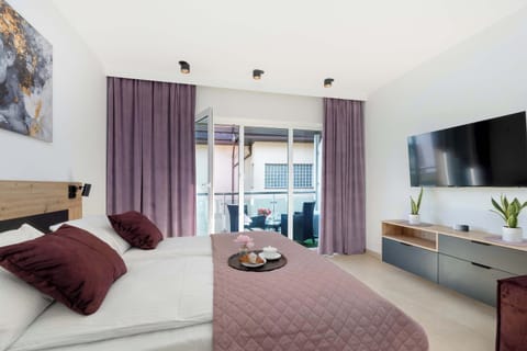Bright studio apartment with a cozy bed, pillows, and large windows – inviting and well-lit relaxation area.