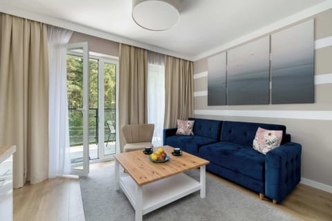 A cozy living room with a navy sofa, coffee table, and access to a balcony through large glass doors. Light wood flooring and striped wall decor give the room a modern, airy look.