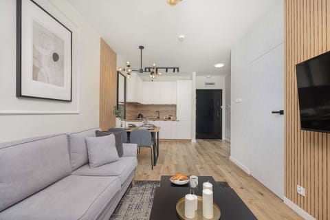 A living room perspective showcasing the gray sofa, a round coffee table, and a framed black-and-white print on the wall. Light walls and wood flooring create an inviting ambiance.

