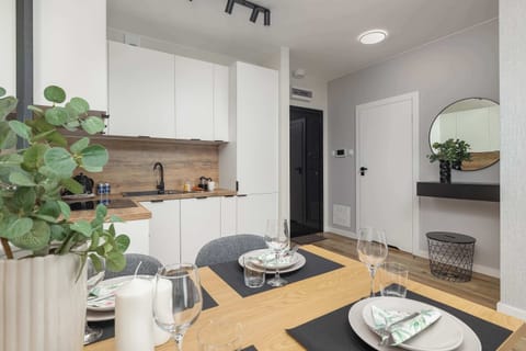 A view toward the hallway and open-plan area, featuring shelves with decorative items and a small dining setup. The entry door and kitchen are visible in the background.

