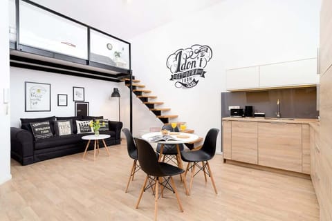 A stylish open-concept living space with a staircase, a kitchen area, and a bold graphic wall design.