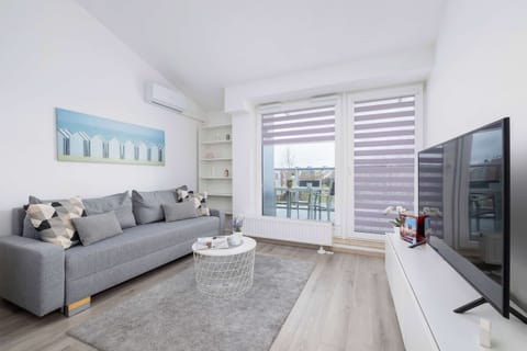  A bright and spacious living room with a comfortable gray sofa, a coffee table, and a large TV. Natural light streams in through large windows, creating an inviting atmosphere.

