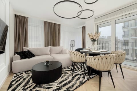 A stylish living room featuring a white curved sofa, a black coffee table, and a modern rug. The decor includes neutral tones and a circular light fixture.