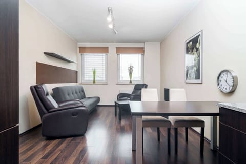 A spacious living room with a comfortable gray sofa and armchair, a TV, and a modern coffee table. The room features dark wood flooring, giving it a cozy and elegant atmosphere.