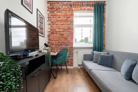 A cozy space with a grey sofa, wall-mounted TV, and a green armchair next to a brick accent wall.