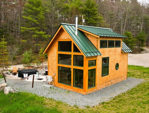 Aerial view of the Willow Cabin, with cedar shingles, forest backdrop, and private hot tub beside the deck.