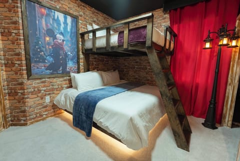 Enjoy a cozy stay in this inviting room with a warm brick wall and soft lighting. The comfortable bedding, striking artwork, and rich red curtains create a unique and charming retreat for a restful night.