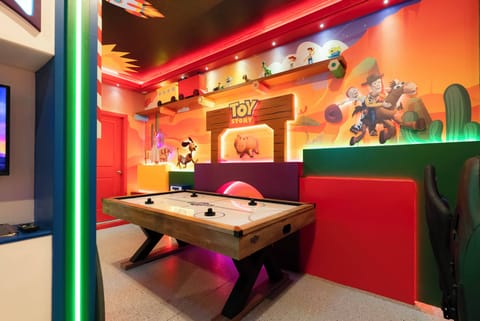 Enter our vibrant game room, featuring bright orange walls with playful murals that set a fun atmosphere. Enjoy friendly competition at the spacious air hockey table, surrounded by colorful accents and lively decor.