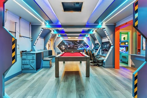 Discover a lively game room featuring a stunning pool table at its heart, enhanced by dynamic blue lighting and modern decor. This inviting space is perfect for friendly competition and relaxation, ideal for fun and leisure.