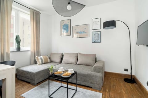 A cozy living room with a stylish sofa, a coffee table, and framed artwork on the walls. The space is bright, with large windows allowing natural light to fill the room.