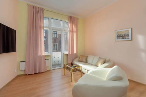 A bright, spacious room with a large window, featuring a double bed, a small coffee table, and two white armchairs.

