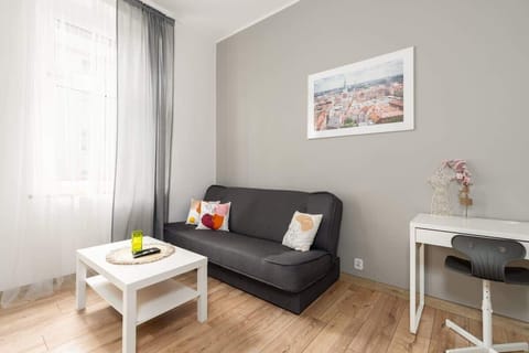 A bright living room with a gray sofa, a white coffee table, and wooden flooring, complemented by natural light from the windows.

