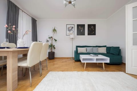 A modern living room with a green sofa, a dining table, and framed artwork on the wall.