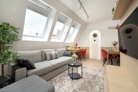 A bright living room with a slanted ceiling, large skylight windows, a gray sectional sofa, and a black wire coffee table next to a small plant.