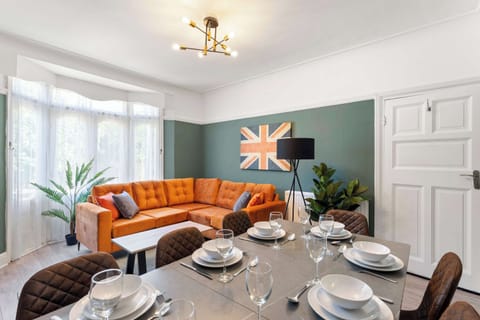 This vibrant space features a sage-green accent wall and a bold orange sectional sofa, with a modern dining table perfectly set for a social meal.
