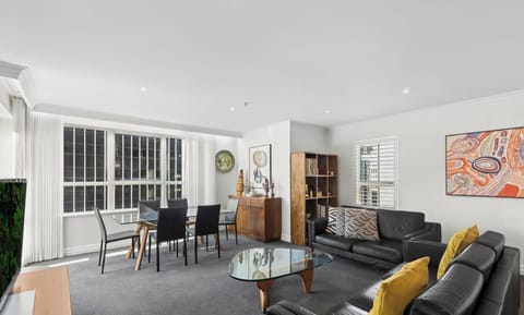 A spacious living room featuring a dark sofa, a glass coffee table, and access to a dining area.