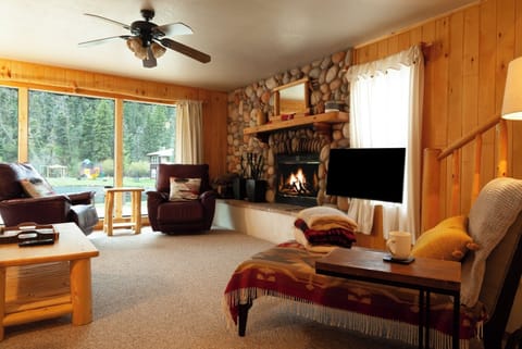 Unwind in your cozy living room with a crackling stone fireplace, warm wood accents, and forest views that invite you to relax and feel truly at home.
