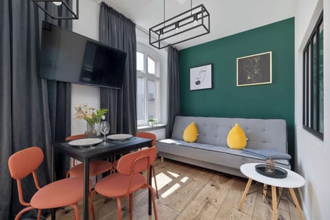 A bright living room with a cozy green wall, orange chairs, and a small coffee table, perfect for relaxing or socializing. Stylish art adds a modern touch to the space.