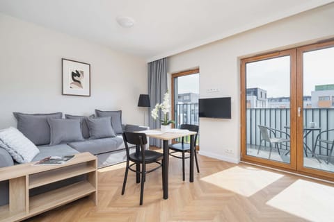 Bright and cozy living space with a grey sofa bed, dining area, and access to the balcony.