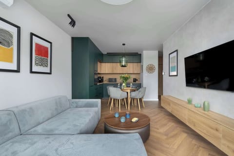 A modern living and dining area with a gray sofa, wooden table, green accent wall, and wall art for a cozy atmosphere.