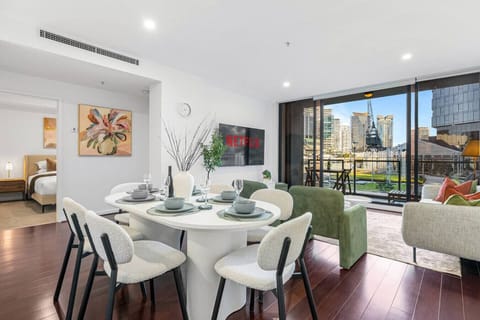 Bright open living and dining area with modern furnishings, a stylish setup for meals, and large glass doors leading to a balcony with stunning waterfront and city views.