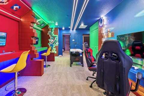 Welcome to a vibrant gaming paradise with bold red and blue walls that set the stage for fun. Relax in sleek gaming chairs and colorful bar stools, creating an energetic atmosphere perfect for entertainment and enjoyment.