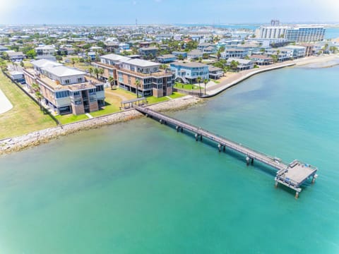 Aerial view showcases waterfront properties along crystal-clear turquoise waters with a private pier extending into the bay.