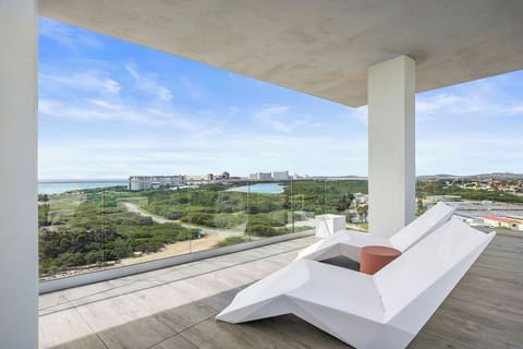 Modern covered terrace with glass railings offering expansive coastal views, greenery, and urban skyline. A shaded outdoor retreat for relaxation and scenic contemplation.