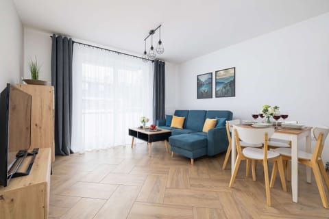 A bright, spacious studio with wooden flooring, a large window, and a modern kitchenette creates a comfortable space for relaxation and daily living.