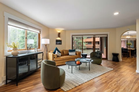 Relax in your spacious living room with warm hardwood floors, cozy seating, and a private balcony overlooking peaceful greenery.