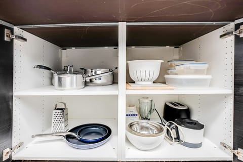 Fully equipped kitchen with essential cookware including pots, pans, and bowls, neatly stored in white cabinets. Features a grater, colander, and various kitchen tools. Everything you need for cooking your favorite meals is right here!