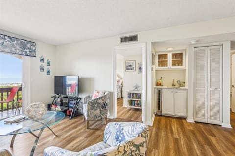 - Living room with TV, stylish chairs and hardwood floors creating a cozy coastal vibe  
- Open layout flows into dining space with balcony access and bright natural light  
- Relax after beach days in comfort with entertainment and seating  