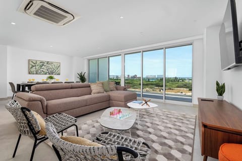 Unwind in your bright, modern living room with sweeping floor-to-ceiling windows framing scenic views of the surrounding landscape. The open layout and stylish furnishings create a welcoming retreat.