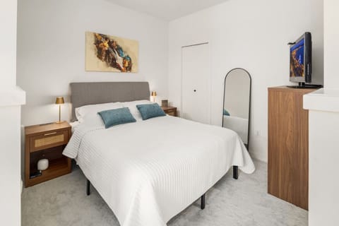 Relax in a cozy bedroom featuring a plush queen-size bed, modern nightstands, soft lighting, and a full-length mirror for added convenience.