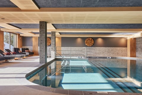 Indoor heated pool with lounge chairs and large windows looking out to the snow-capped peaks — included in every stay.