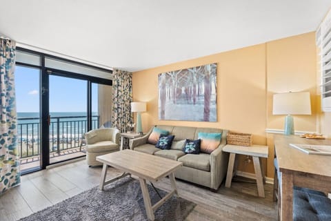 Oceanfront living room at Beach Cove Resort in North Myrtle Beach with balcony views, comfy sofa, chair, dining space, and queen sleeper sofa; perfect for relaxing and enjoying your coastal getaway. All essentials for a top resort experience!