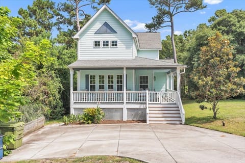 Charming coastal cottage featuring mint green siding and wraparound porch surrounded by lush trees.