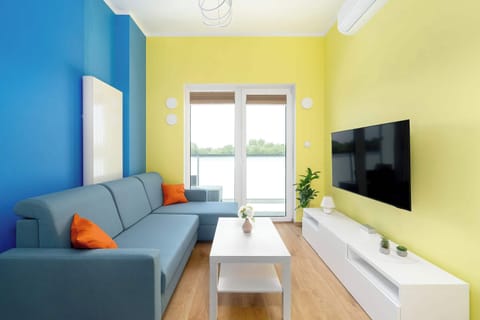 A cozy living room with a light blue couch, yellow walls, a TV, and access to a balcony through wide glass doors.