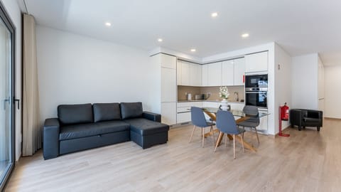 Modern and bright open-plan living area with a stylish sofa, dining space, and fully equipped kitchen. Perfect for relaxing after a day at the beach. #ModernLiving #QuarteiraApartment #OpenPlanDesign