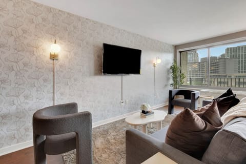 Open living room with sculptural accent chairs, a sleeper sofa, and wall-to-wall city views — comfortable seating for the whole group with room to spare.