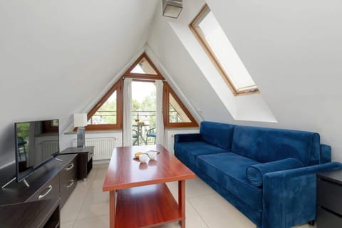 Bright and cozy living area with a sloped ceiling, stylish blue corner sofa, wood coffee table, and elegant accents.