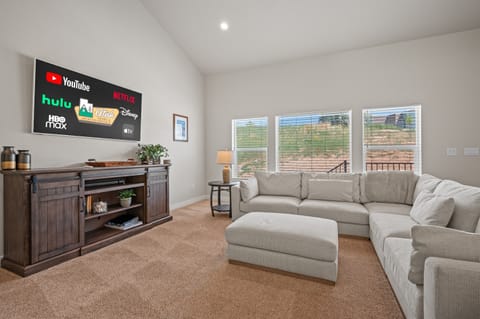 Relax in the inviting living room featuring a plush sectional, ottoman, big-screen TV for streaming, and a trio of windows that fill the space with light.
