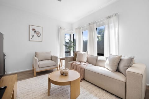 Unwind in the sunlit living area with a plush sofa, accent chair, large-screen TV, and calming neutral décor, perfect for slow mornings or relaxed evenings.