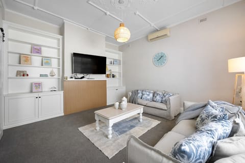 Unwind in the main living area, featuring two plush sofas, a Smart TV with streaming apps, split-system air conditioning, and a curated bookshelf.