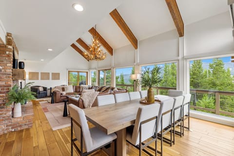 Gather around the stunning dining table beneath soaring beamed ceilings with breathtaking mountain views. The open layout flows seamlessly to a cozy living area with a warm fireplace.