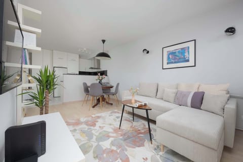 A bright and modern living room featuring a comfortable sofa, a stylish rug, and a workspace with a desk and chair. Natural light fills the room, creating a welcoming atmosphere.