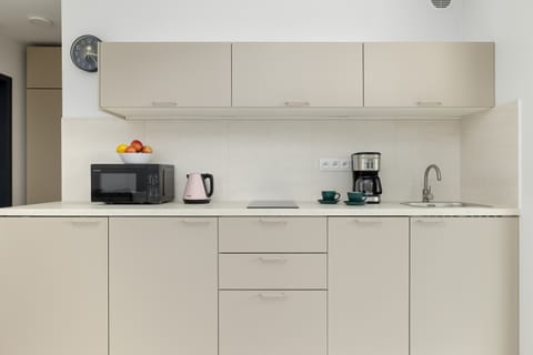 A small kitchen with white cabinetry, a toaster, microwave, kettle, and coffee machine placed neatly on the counter.