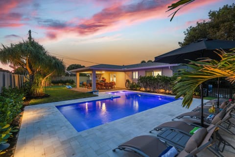 End the day poolside under pink South Florida skies, with glowing water, lounge chairs, umbrellas, and cornhole ready for an easy evening outdoors.