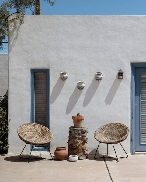 A peaceful patio setup with woven chairs, terracotta pots, and a classic stucco wall.