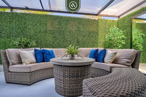 Cozy outdoor terrace featuring circular wicker sofas, blue accent pillows, and a lush artificial green wall.